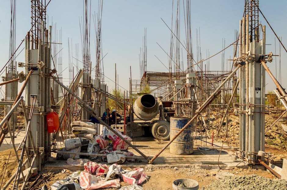 Industrial construction site featuring cement mixer, steel columns, and scaffolding.