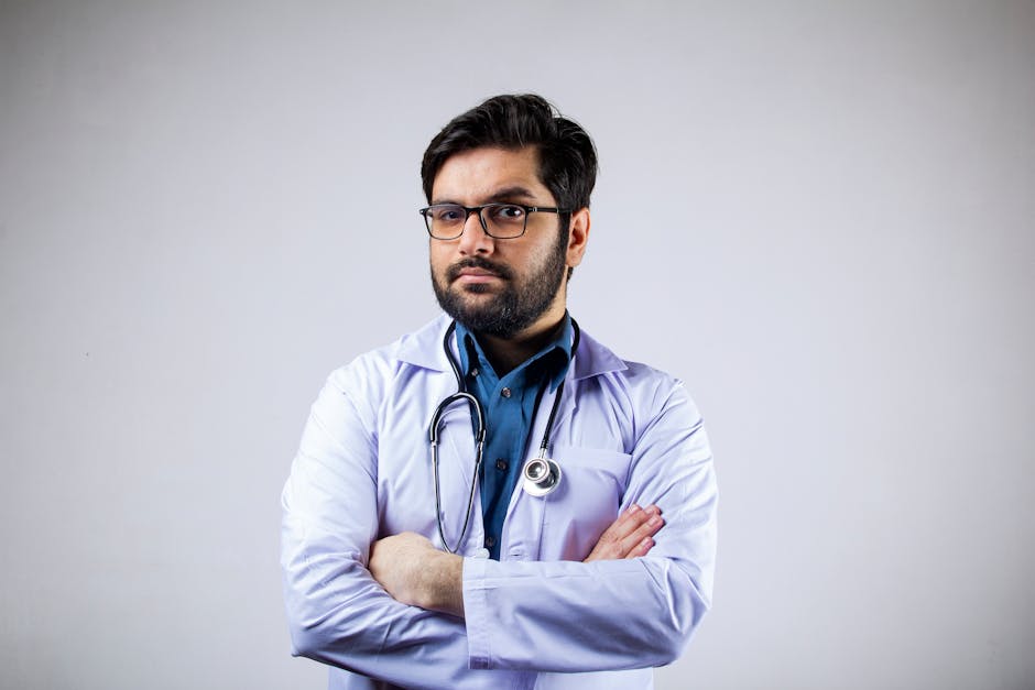 Portrait of a serious male doctor in a white coat with arms crossed, wearing glasses and a stethoscope